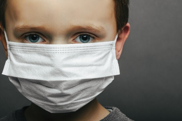 Face of a mask-wearing boy with fear in the eye Close-up on a gray surface.
Coronavirus and Air pollution pm2.5 concept