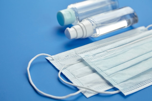 Face masks and bottles of antibacterial hand sanitizer on blue background