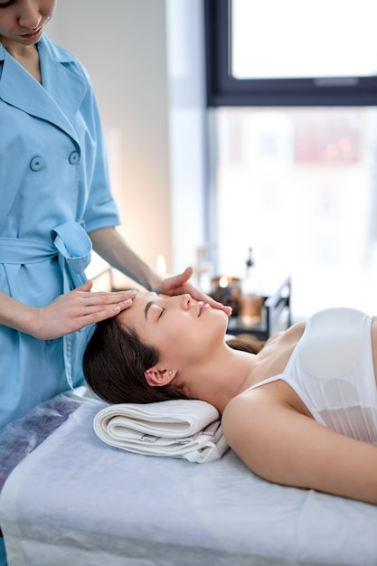 Face massage. Asian young woman getting spa treatment by masseur, side view