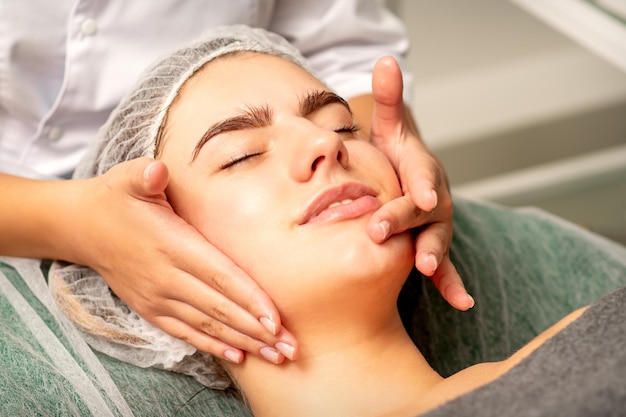 Face massage Beautiful caucasian young white woman having a facial massage with closed eyes in a spa salon