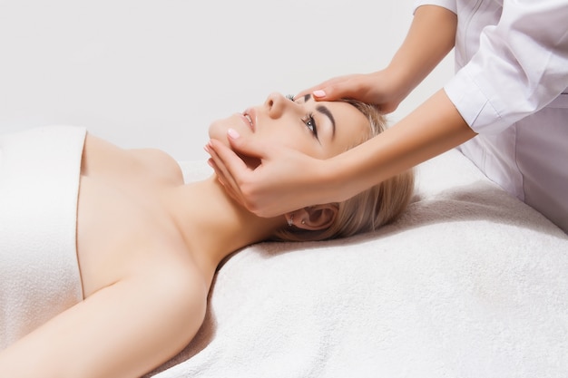 Massaggio viso. primo piano di una giovane donna che riceve il massaggio spa in un salone di bellezza e spa da estetista. spa cura della pelle e del corpo. cura del viso di bellezza. cosmetologia.