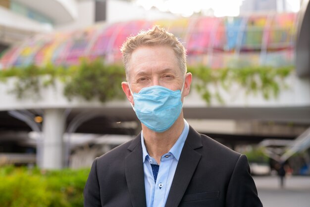 Face of mature businessman wearing mask for protection from coronavirus outbreak in the city streets