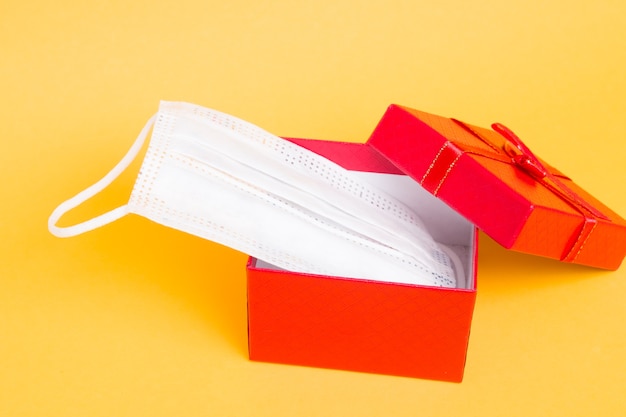 face medical mask and red gift box on a yellow background copy space