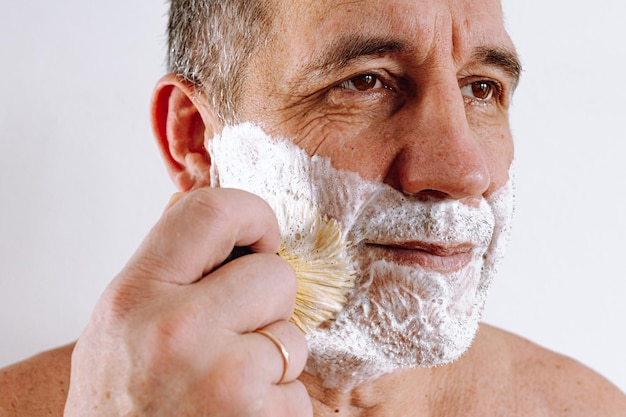 Photo face of middle-aged man close-up, brown eyes, with stubble on face, lathered with shaving foam