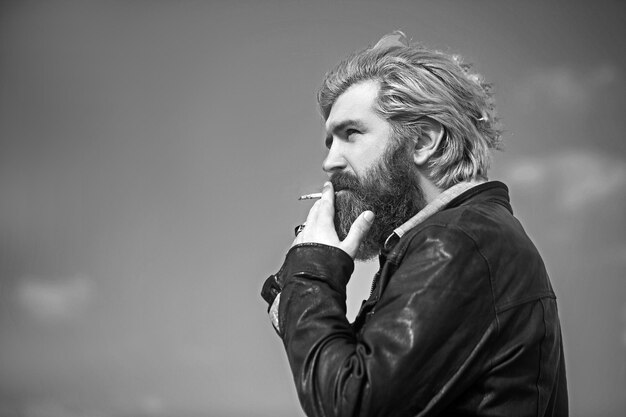 Photo face of a middle aged man smoking a cigarette and looking thoughtful set against a blue sky