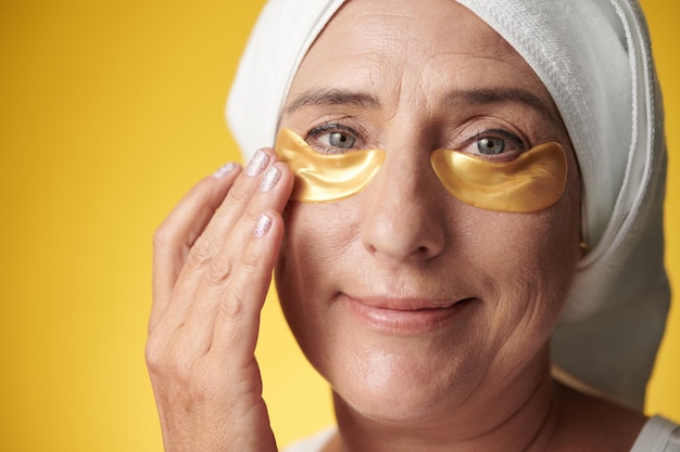 Photo face of middleaged woman applying moisturizing eye patches and smiling at camera