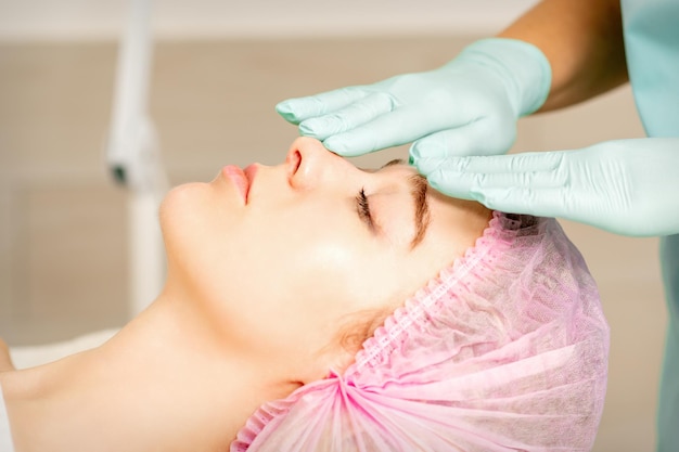 Face peeling at the beautician. Facial treatment. The beautician applies a cleansing face mask to the female patient.