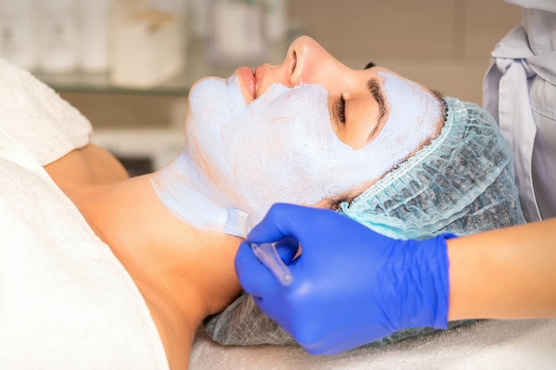 Face peeling at the beautician. facial treatment. the beautician applies a cleansing face mask to the female patient