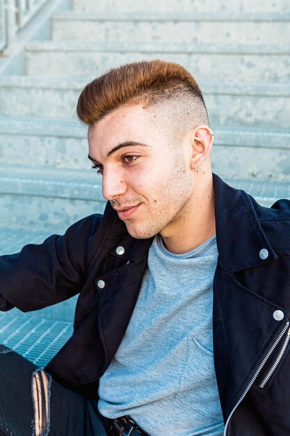 Face portrait of a handsome young and rocker man sitting on stairs in the street