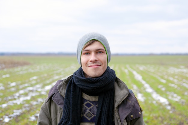 Face portrait of a young guy 21-22 years old against a background of green snowy spring grass.