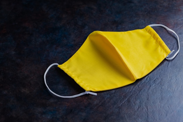 Face protective mask. Reusable antivirus mask made from yellow cotton. Yellow protective mask on a dark background. Eco-friendly tailoring. Top view. Copy space