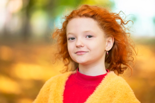 The face of a redhaired girl closeup against the background of an autumn park Child in autumn