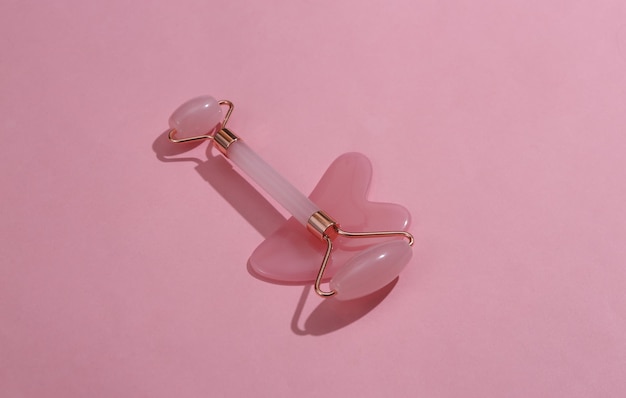 Face roller and gua sha stone massager on pink background Top view