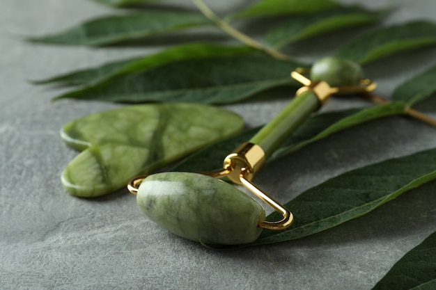 Face roller, gua sha and twig on gray textured background