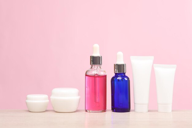 Face serum bottles cream tubes and jars on the table pink background Skin health and youth concept