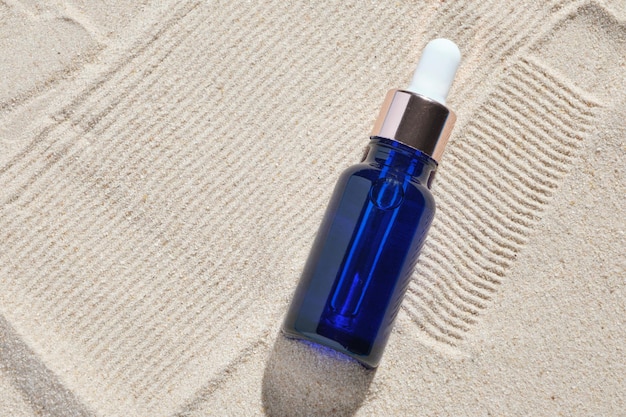 Face serum of glass bottle with a pipette on a natural background with sand Essential oil for moisturizing body skin mockup of beauty fashion cosmetic bottle dropper product with skincare concept