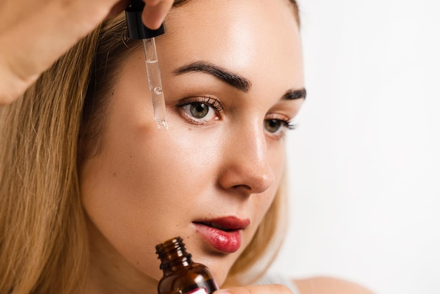 Face serum pipette closeup with attractive girl on white background Girl applies face serum to her face with pipette on white background