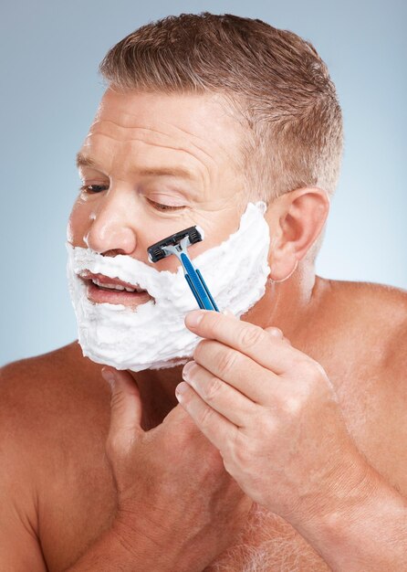 Face shaving cream and man with razor in studio isolated on a gray background for hair removal Cleaning skincare and senior male model with facial foam to shave for aesthetics health or wellness