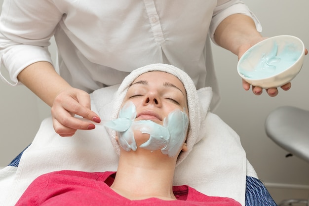 Face skin care. Beautician applying beauty oil mask on face using brush In spa salon