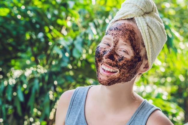 Photo face skin scrub. portrait of sexy smiling female model applying natural coffee mask, face scrub on facial skin. closeup of beautiful happy woman with face covered with beauty product. high resolution