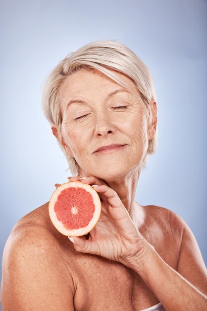 Фото Уход за кожей лица и пожилая женщина с грейпфрутом изолированы на синем фоне студии счастливая пожилая и женская модель с закрытыми глазами, держащая фрукты для естественного ухода за лицом, здоровая кожа или витамин с