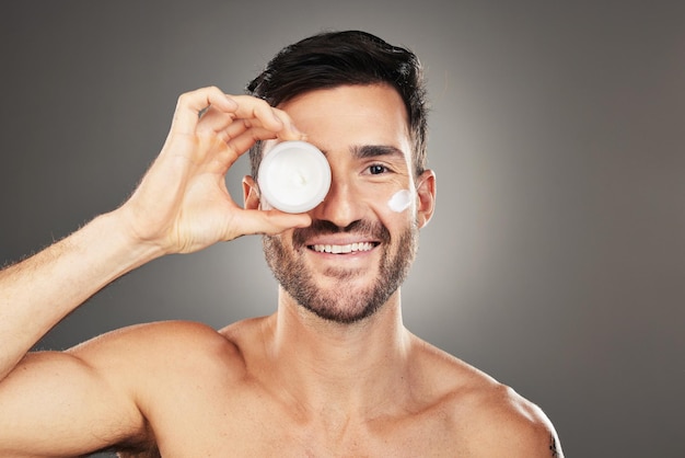 Face skincare and product with a man model in studio on a gray background to promote beauty treatment Portrait container and antiaging with a handsome young male posing for wellness or care