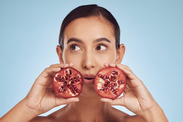 Face skincare and woman with pomegranate for beauty in studio isolated on a blue background Natural cosmetic fruit and model with food for nutrition healthy vegan diet and vitamin c for wellness