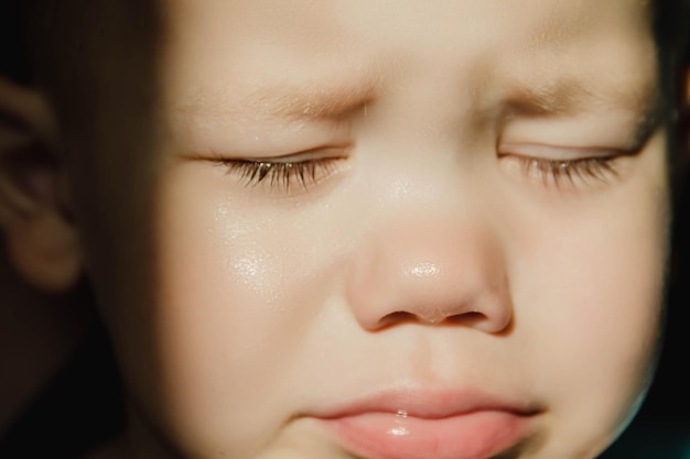 Лицо маленького ребенка, который плачет с закрытыми глазами и выпяченной губой