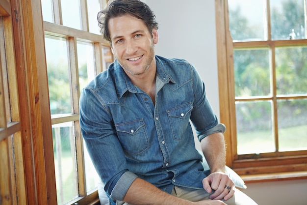 face smile and portrait with man in home sitting alone by window with happiness in lounge homeowner confidence and morning relax with handsome young male on windowsill in modern england house