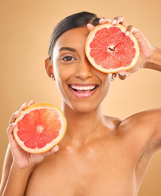 Foto viso sorriso cura della pelle e donna con pompelmo in studio isolato su sfondo marrone ritratto cosmetici naturali e felice modello femminile indiano con agrumi per vitamina c nutrizione o bellezza