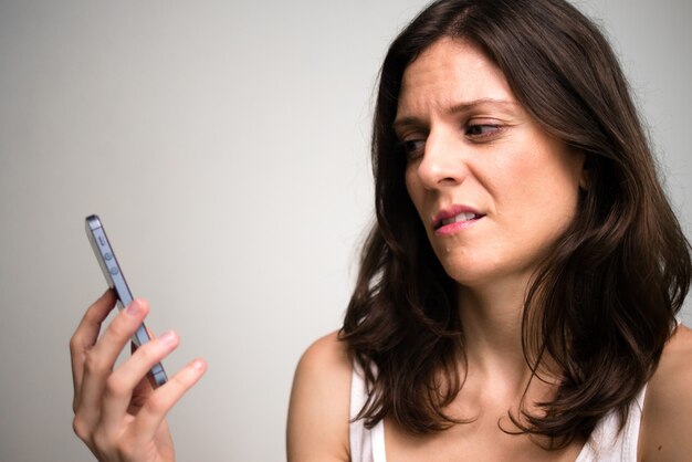 Лицо подчеркнутой женщины с отвращением смотрит на телефон