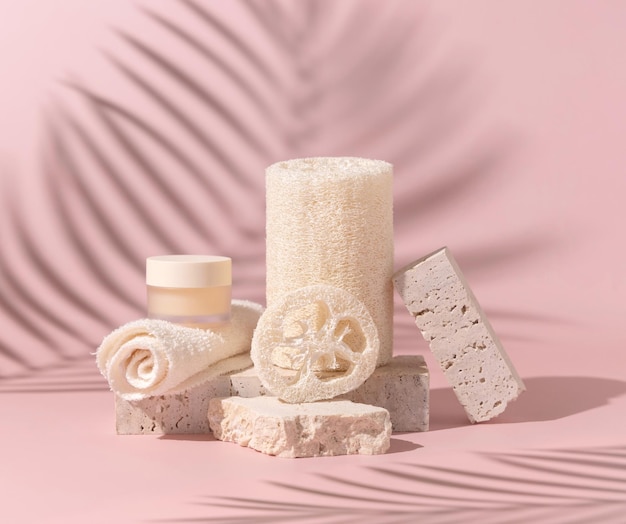 Face towel loofah sponges and cream jar on stones on light beige close up Mockup