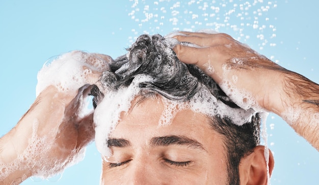 Face water splash and shampoo shower of man in studio isolated on a blue background Water drops hair care and male model washing bathing or cleaning for healthy skin wellness or skincare hygiene