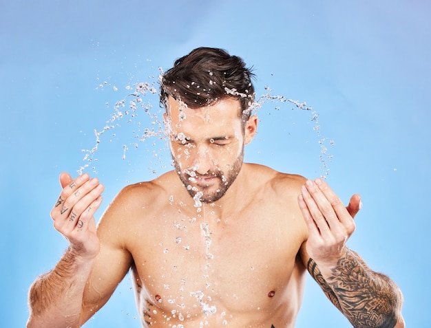 Face water and splash with a man cleaning his skin in studio on a blue background for hygiene or hydration Wellness skincare and water splash with a handsome young male washing his body for care