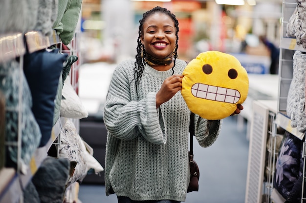 Face with teeth emoji. African woman with pillow in a modern home furnishings store.