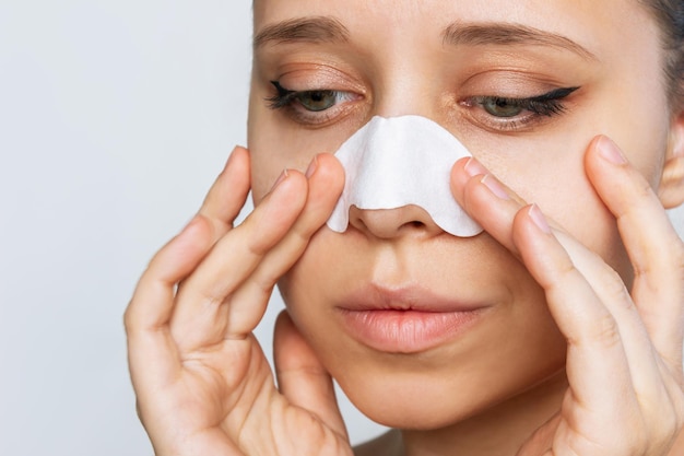 A face of woman cleaning a skin of her nose with strips from blackheads or black dots Acne problem