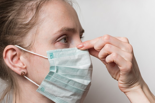 Face of woman in medical mask. Girl presses protective mask to nose. Protection for influenza virus