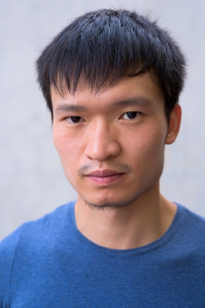 Face of young Asian man against concrete wall