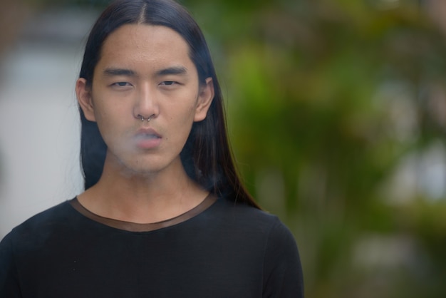 공원에서 긴 머리 흡연을 가진 젊은 아시아 남자의 얼굴