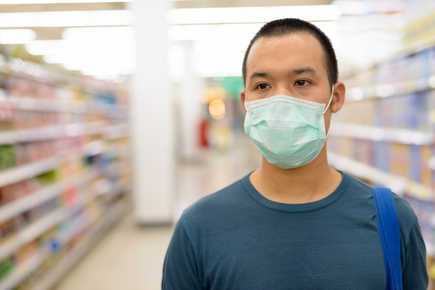 Face of young Asian man with mask shopping with distance at the supermarket