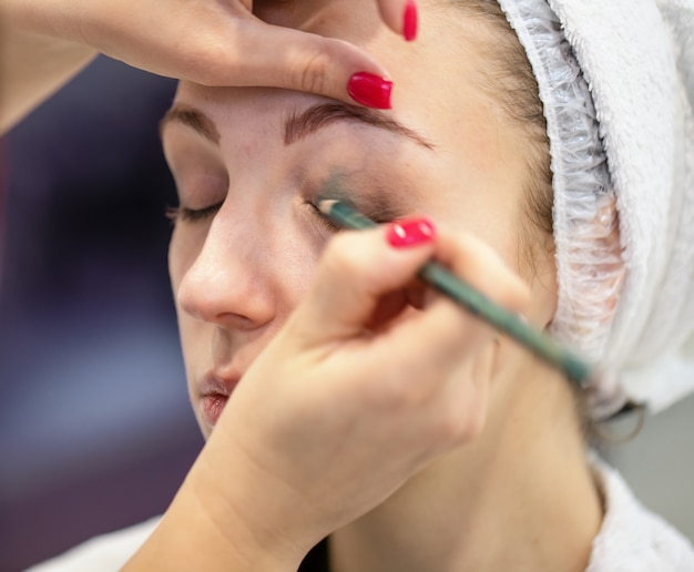 Face of young girl with hands of makeup artist applying makeup