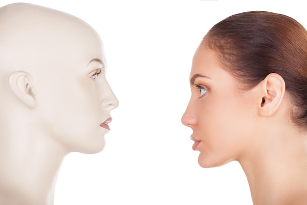 Face your problem. Side view of beautiful young woman standing in front of the mannequin and looking at it while standing isolated on white background