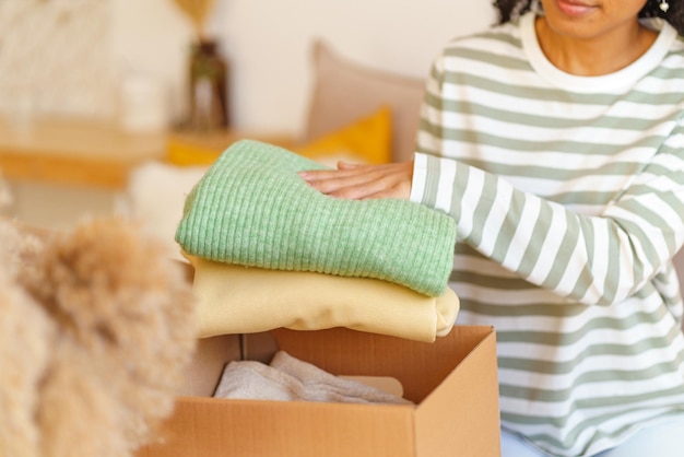 Photo faceless ethnic female putting clothes in box concept of moving house and packing stuff