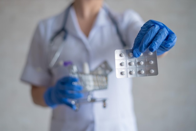 Foto una dottoressa senza volto in guanti di gomma mostra un blister con pillole e tiene in mano un mini carrello con un pacchetto completo di medicinali diversi raccomandazioni del farmacista