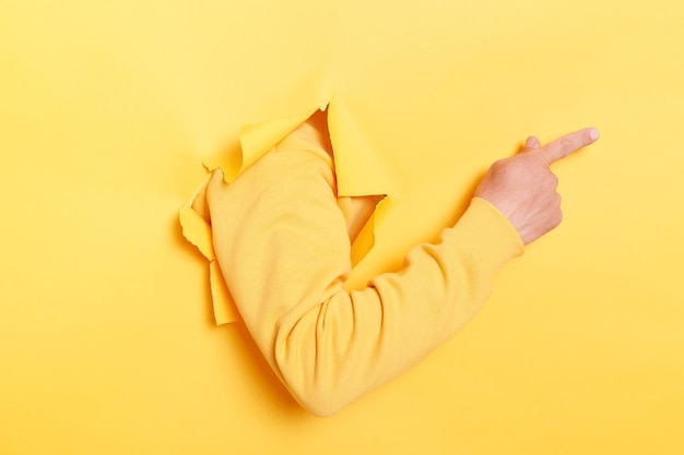 Faceless human breaks arm through paper yellow wall indicates on right at blank space gives advice to buy subscription suggests to click on link showing direction Place for your advertisement