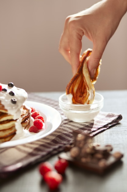 朝食を持っている人の顔のない画像は、パンケーキをサワークリームに浸します。