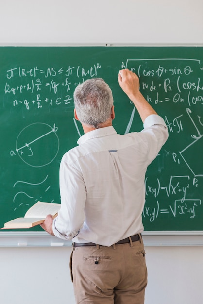 Photo faceless lecturer chalking formula on blackboard