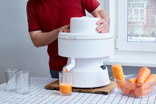 Faceless man squeezes carrot juice in a white professional juicer.