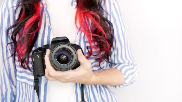 Faceless nice woman with brown red hair in a tshirt with hands holding photo camera white background