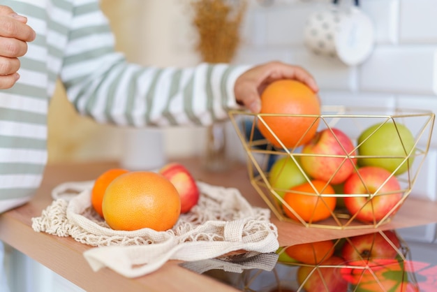 Faceless person grabbing ripe apple from fruit bowl on kitchen table sorting after grocery store